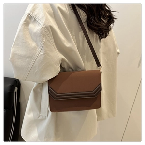 Sac bandoulière marron avec bordure en V portée par un mannequin dans un décor sobre