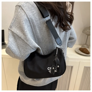 Detail of black nylon hobo bag with wide shoulder strap worn by model in cozy room