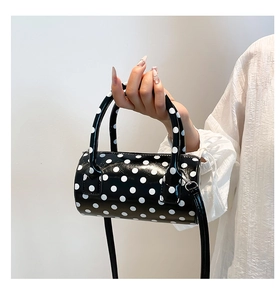 Chic black cylinder handbag with white polka dots held by model against white wall
