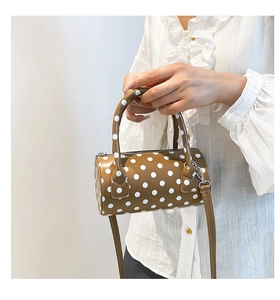 Close-up of a brown polka dot cylindrical handbag with leather handles and crossbody strap