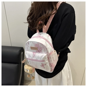 Detailansicht eines Mini-Rucksacks mit rosa Schmetterlingen und flauschigem Monster-Anhänger