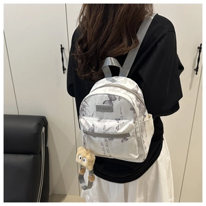 Detailansicht des Mini-Rucksacks in Weiß mit Schmetterlingsdruck und Plüschbär-Anhänger