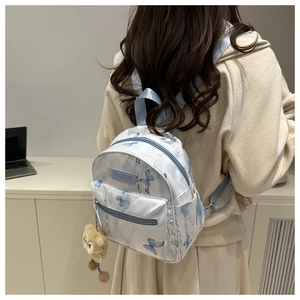 Close-up of mini backpack with butterfly print, logo patch, and plush bear charm accessory