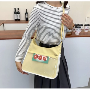 Close-up of a pale yellow crossbody bag with a transparent PVC front pocket and flower card