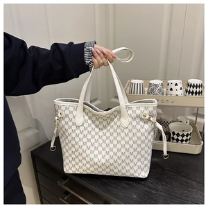 Detail of white tote bag with grey M-letter print and golden hardware in lifestyle setting