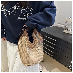 Detail of woven straw tote bag featuring brown leather trim and round hanging charm