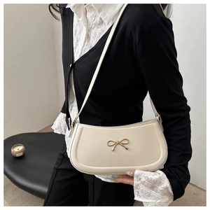 Detail showing creamy white shoulder bag with a thin gold bow buckle on the strap