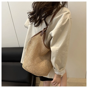 Detail of a large straw tote bag with brown leather handles worn by a model in a stylish room