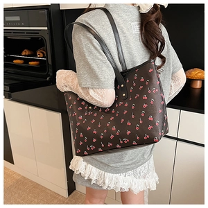 Detail of dark tote bag with cherry print and golden studs worn by model in a kitchen