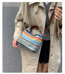 Détail d'un sac seau en paille tissée colorée avec bandoulière en cuir sur trench
