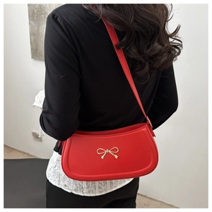 Detailed view of red underarm bag with a golden bow on a model against white wall