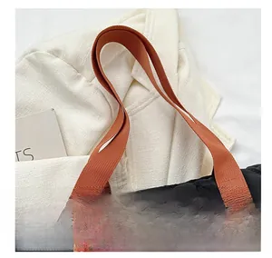 Detail of black quilted tote bag featuring high-contrast orange nylon webbing handles