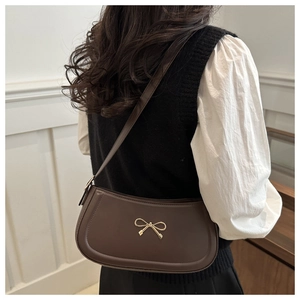 Detail view of brown leather underarm bag with gold bow clasp and sleek stitching