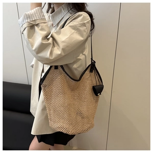 Dettaglio della borsa tote in paglia con finiture e tracolla in pelle nera indossata dal modello