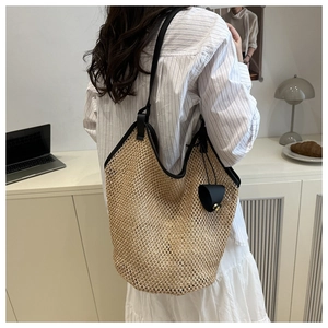 Detail of a large woven tote bag with black leather straps on a model in a cozy setting