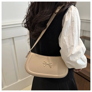 Detail of beige shoulder bag featuring a gold bow metallic clasp on a textured surface