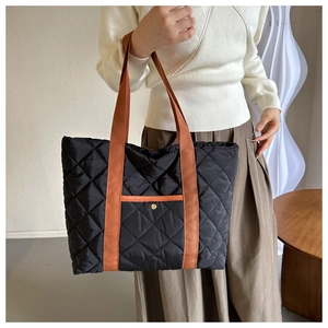 Black quilted tote bag with brown handles and front pocket shown in a minimalist setting