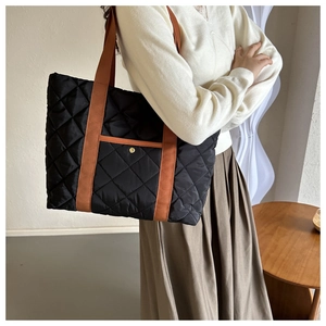 Detail of black quilted tote bag with brown straps and golden buckle on front pocket