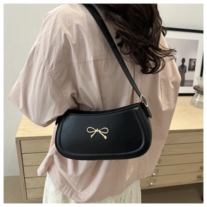 Detailed view of black PU leather underarm bag with gold bow clasp on a model's shoulder