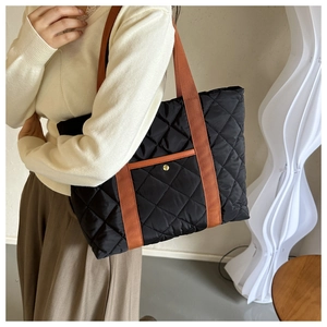 Detail of a black quilted tote bag with brown straps and a gold button front pocket
