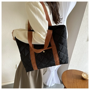Detail showing the black quilted pattern and durable reddish-brown woven straps of the tote bag