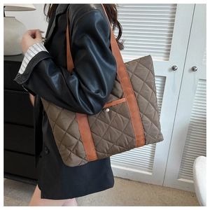 Detail of brown quilted tote bag showing wide orange strap and metal snap pocket detail