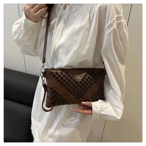 Detail of dark brown leather crossbody bag with black rivets held by model in white dress