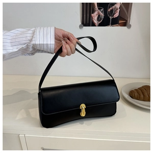 Detail shot of a black minimalist underarm bag with gold metal clasp on a white table