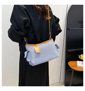 Detail of light blue denim crossbody bag with brown leather trim and utility side pockets