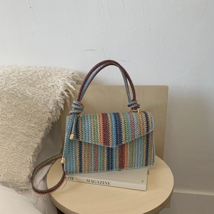 Colorful woven crossbody bag with striped pattern and gold hardware on a wooden stool