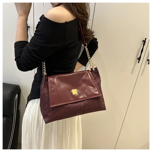Detail of burgundy leather tote featuring snake pattern embossing and gold chain strap