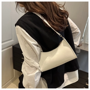 Close-up of minimalist cream patent leather underarm bag worn on shoulder by model
