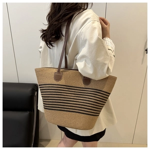 Detail shot of woven straw tote bag with black stripes and brown leather shoulder straps