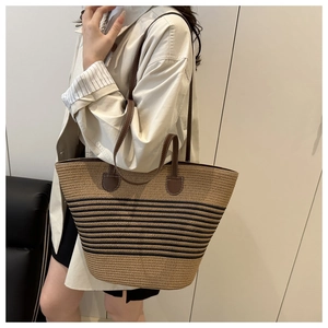 Detail of woven straw bucket bag with contrasting black stripes and brown leather strap