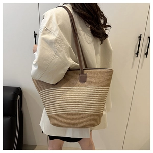 Close-up of a striped woven straw tote bag with brown leather handles worn on shoulder