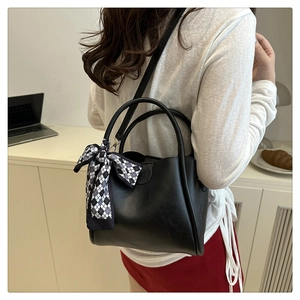Modern black leather bucket bag with silk scarf accessory shown in a lifestyle office setting