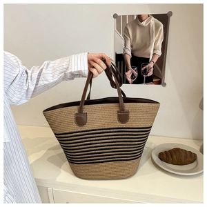 Close-up of hand-woven straw tote bag featuring black stripes and brown leather handles