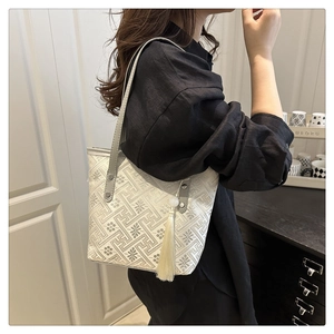 Detail of embroidered tote bag with geometric patterns, leather handles and white tassel