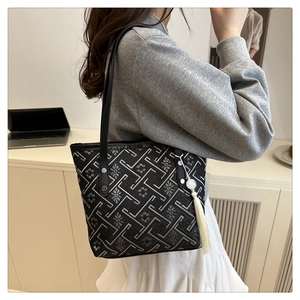 Dettaglio borsa tote nera con ricami geometrici e nappa indossata a spalla da modella