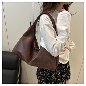 Detail view of large dark brown tote bag with leather texture shown on shoulder
