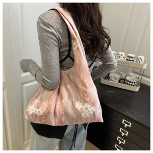 Detail of floral embroidery on a pink tie-dye tote bag worn by a model in lifestyle setting