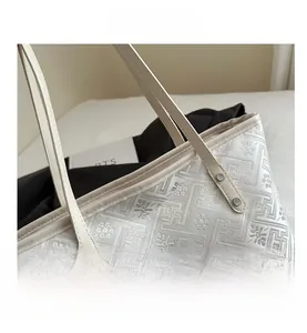 Close-up of beige tote bag featuring geometric patterns and floral embossed texture