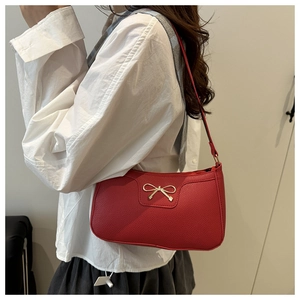 Close-up of a red shoulder bag with lychee texture and a gold bow buckle on white shirt