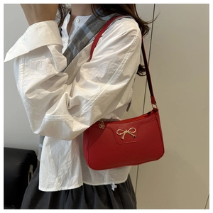 Detail of red pebbled leather shoulder bag featuring a gold bow and flower zipper