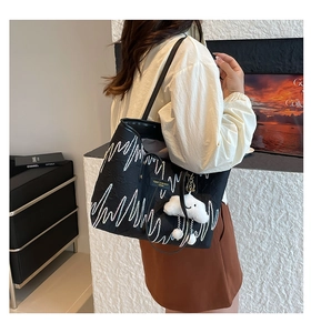 Detail of black striped tote bag with wave embroidery and plush cloud charm accessory