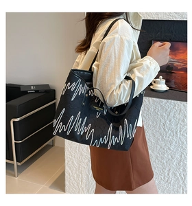Detail view of black tote bag with embossed wavy patterns and slim shoulder straps