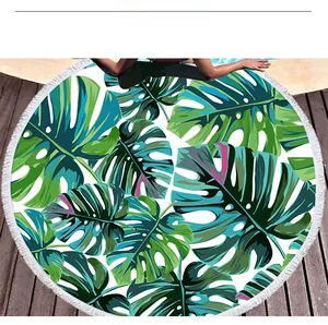 Detail of round beach towel with green monstera leaf print and white fringe tassels