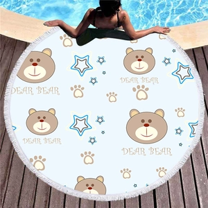 Round beach towel with cute cartoon bear pattern and tassels on a wooden pool deck