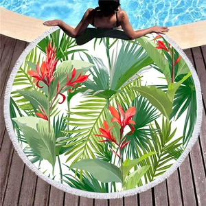 Circular beach towel with tropical floral prints and white tassels on a poolside deck