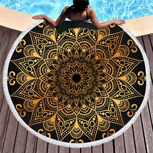 Black and gold mandala round beach towel with white tassels on a wooden pool deck